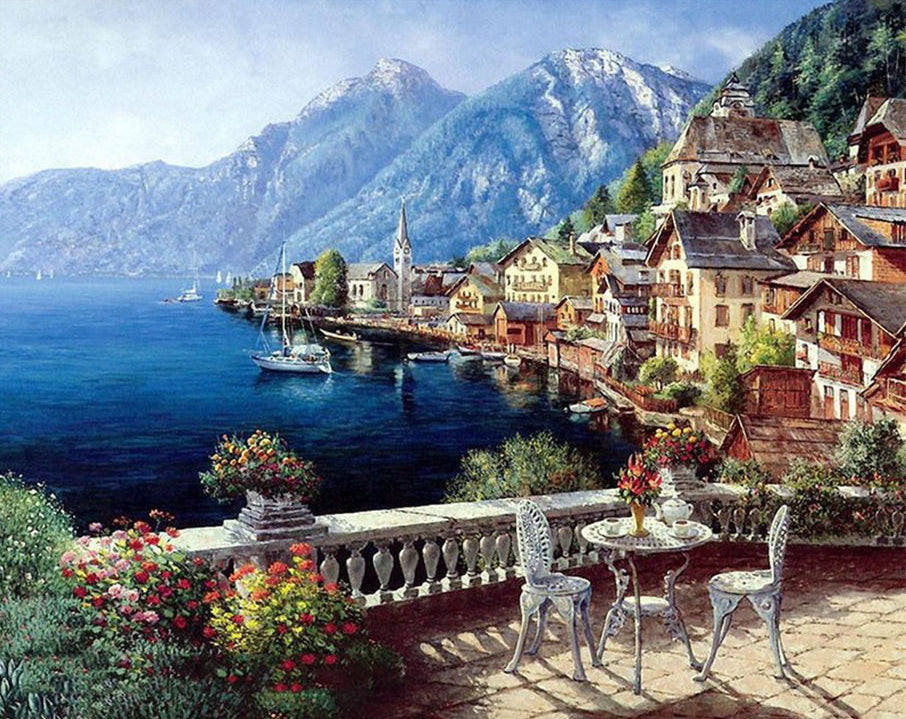 Scenic view of a lakeside village with mountains and a table with chairs.